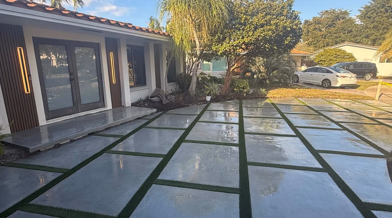 Large concrete slab driveway with artificial turf joints in front of a modern entry with LED sconces.