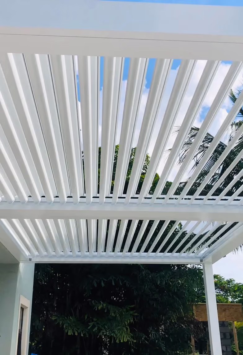 White louvered roof blades tilted open seen from below with palm trees and sky beyond