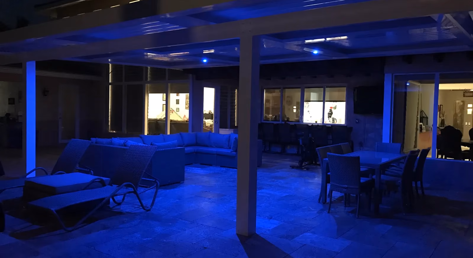 Outdoor lounge and dining set under a louvered roof washed in blue LED light at night