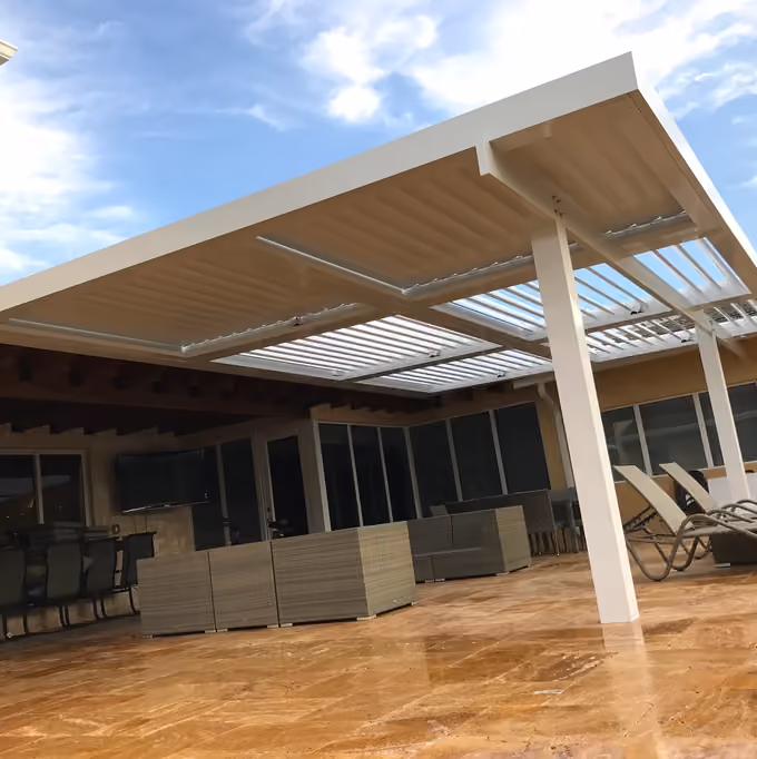 Large white louvered roof with partly open blades over a travertine patio with wicker lounge furniture