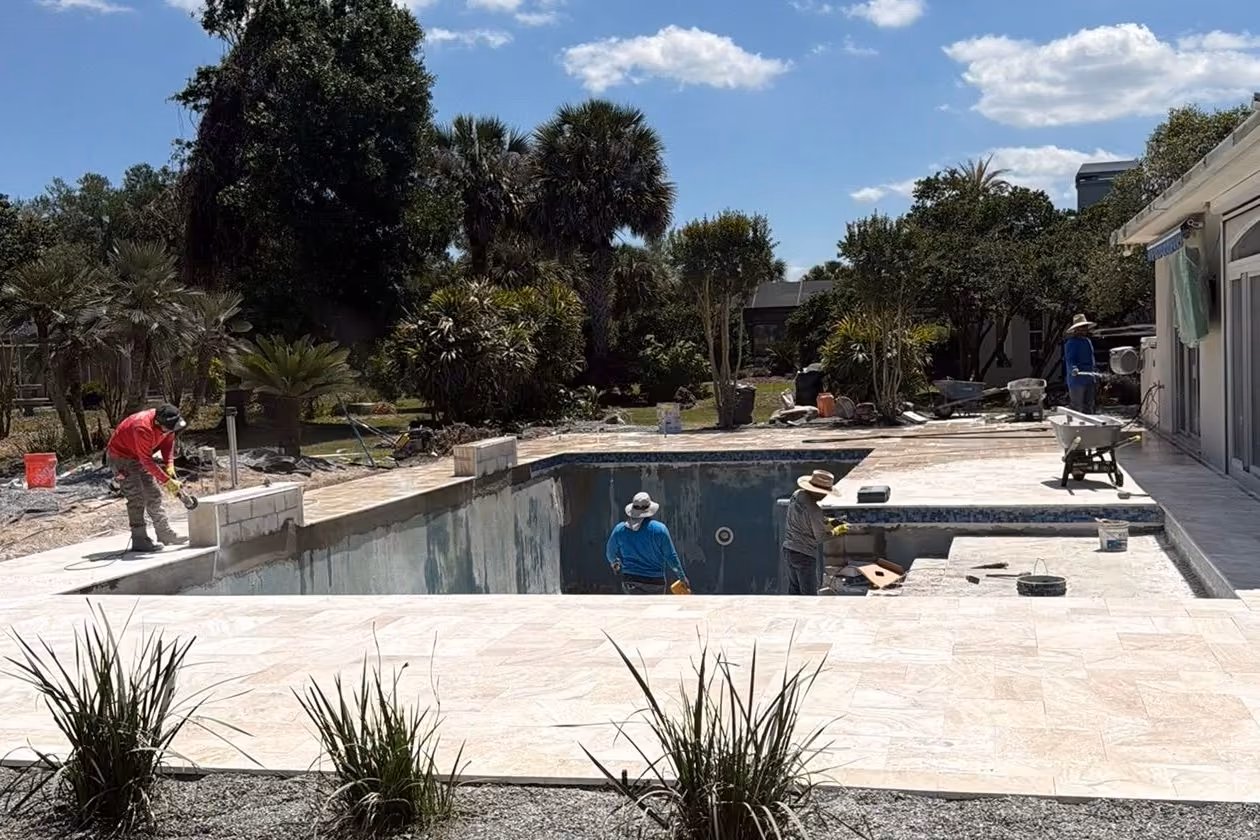 Crew cutting block and setting the deck around a drained pool during a pool remodeling project in Florida