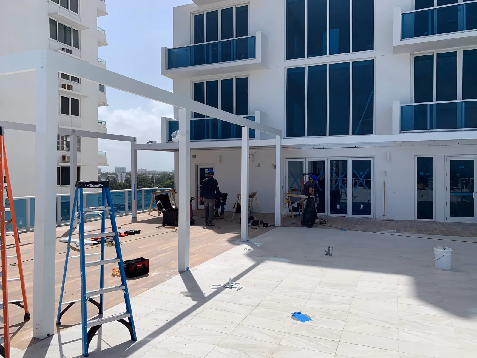 Crew assembling white pergola posts and beams on a condominium pool terrace.