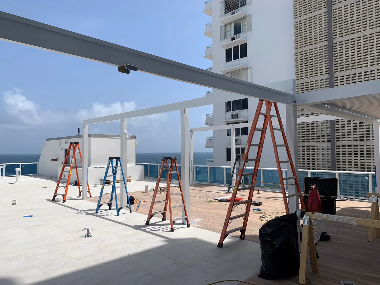 White pergola frames and ladders on a rooftop terrace with the ocean behind.