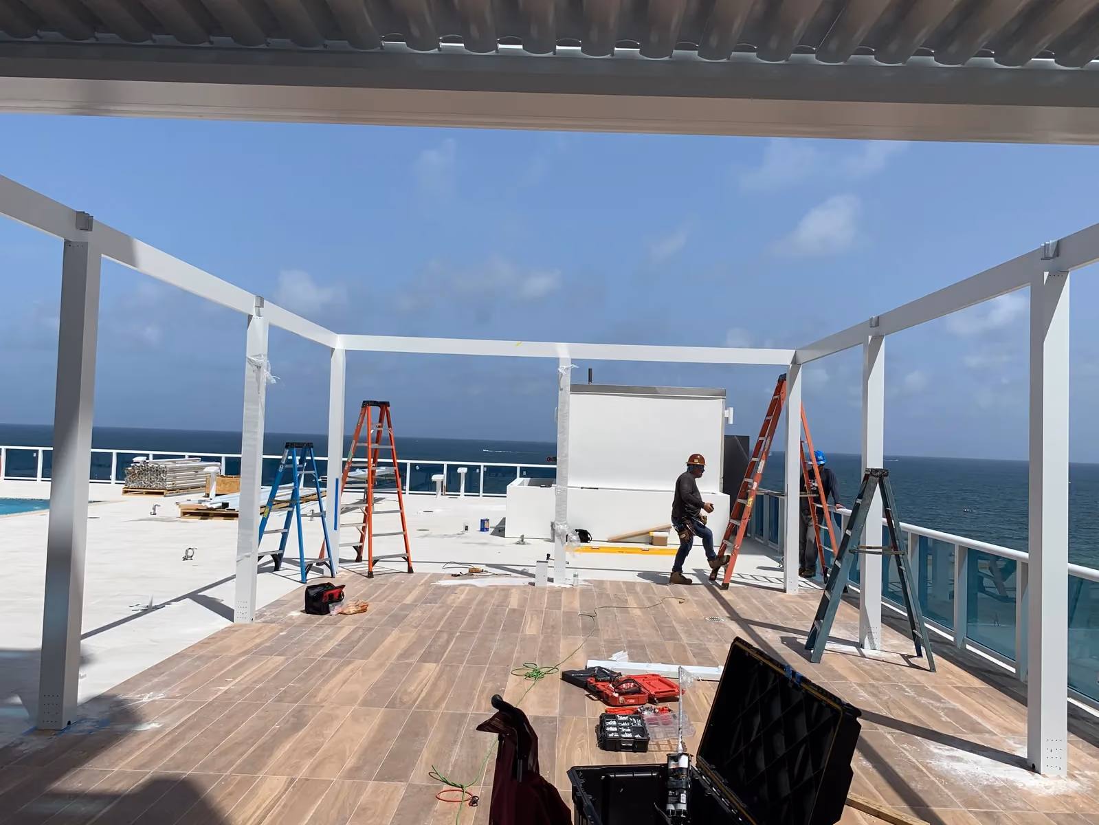 White louvered pergola frame being assembled on an oceanfront rooftop deck.