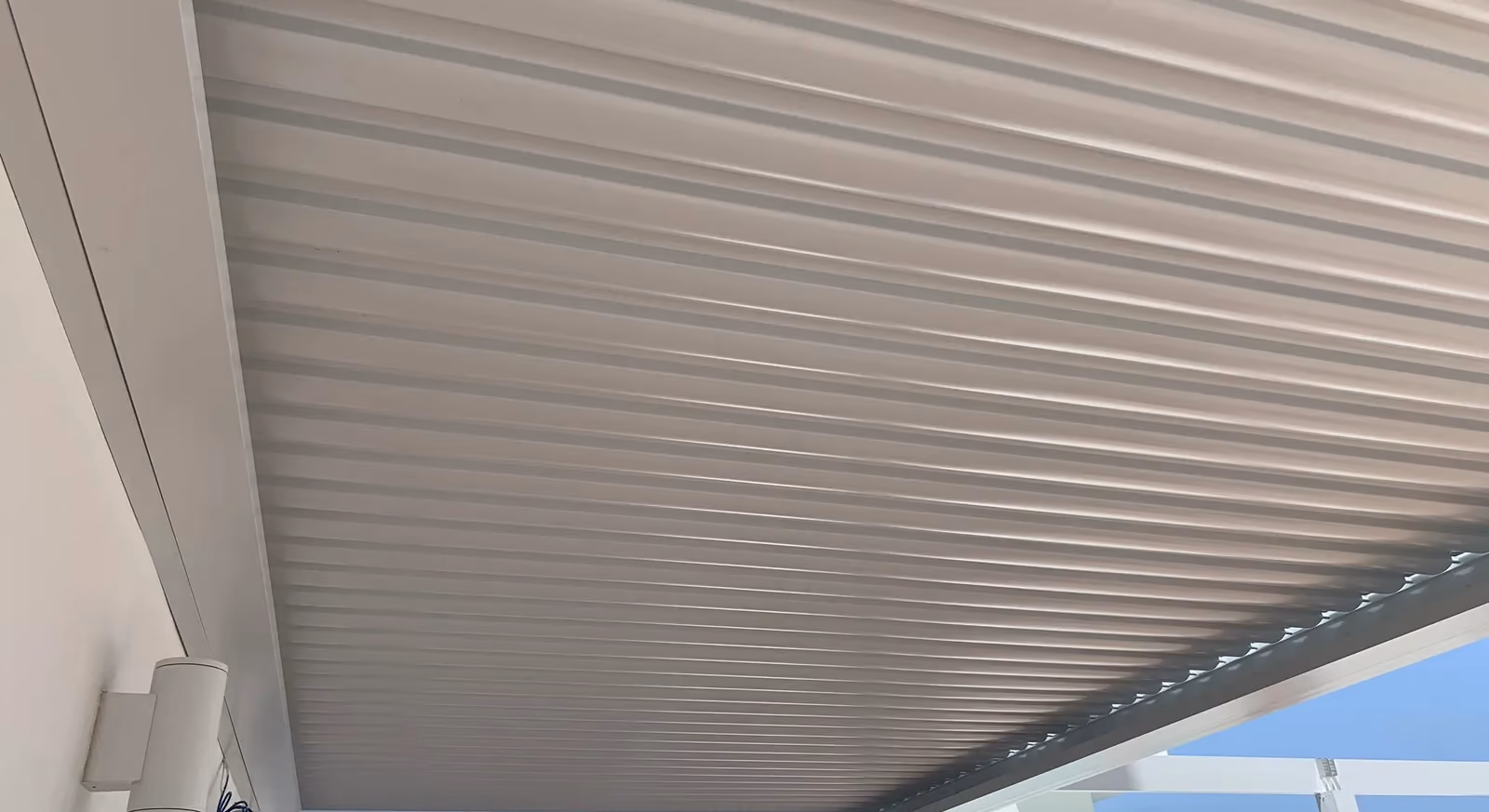 Underside of a white louvered roof with louvers closed, wall lights on the left.