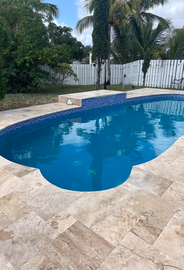 Remodeled freeform pool with blue mosaic waterline tile and travertine deck.
