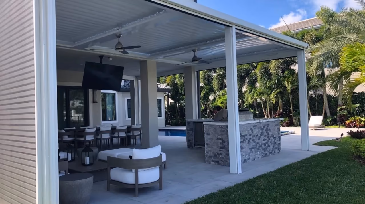 White louvered pergola covering an outdoor kitchen with stacked stone island and lounge seating.