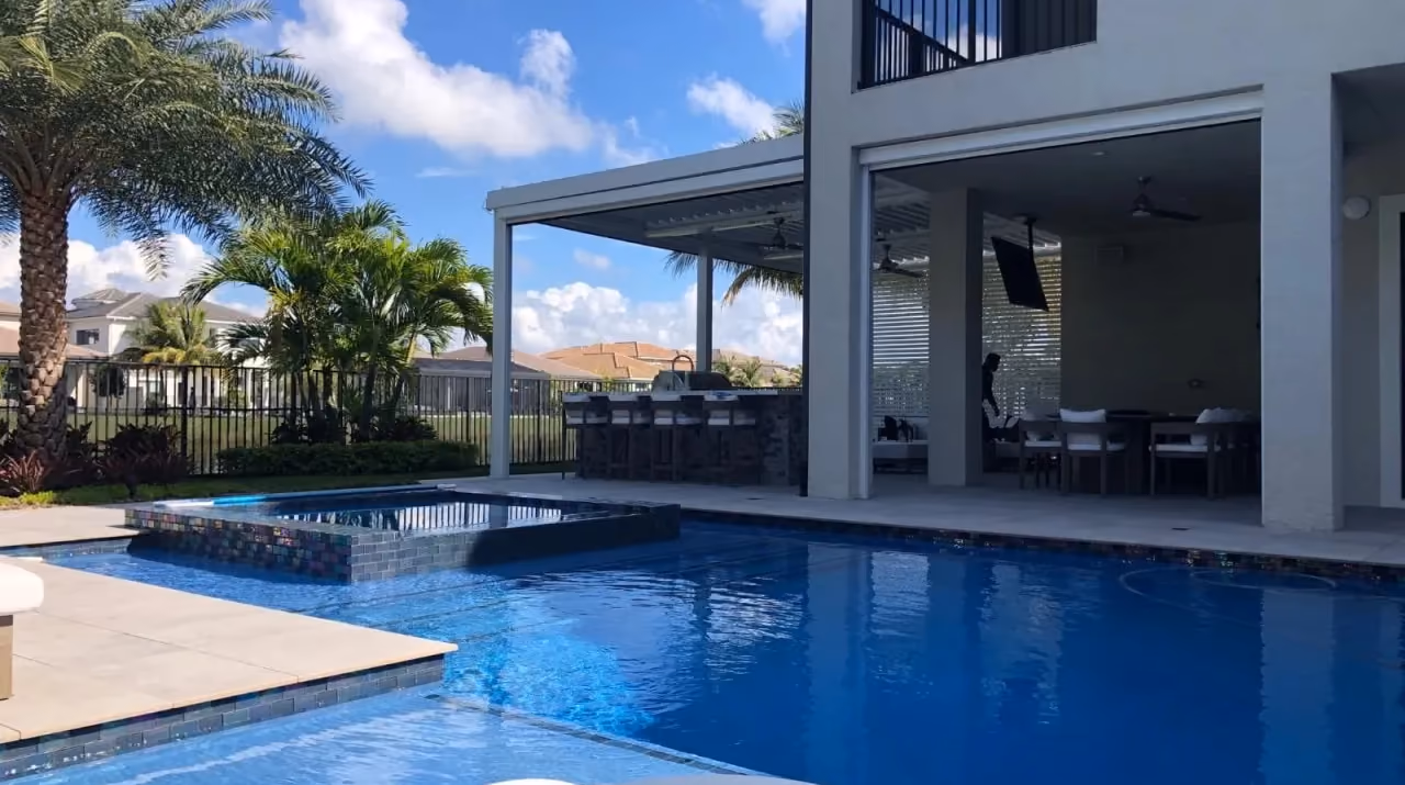 Pool with raised glass-tile spa in front of a louvered pergola and outdoor bar.