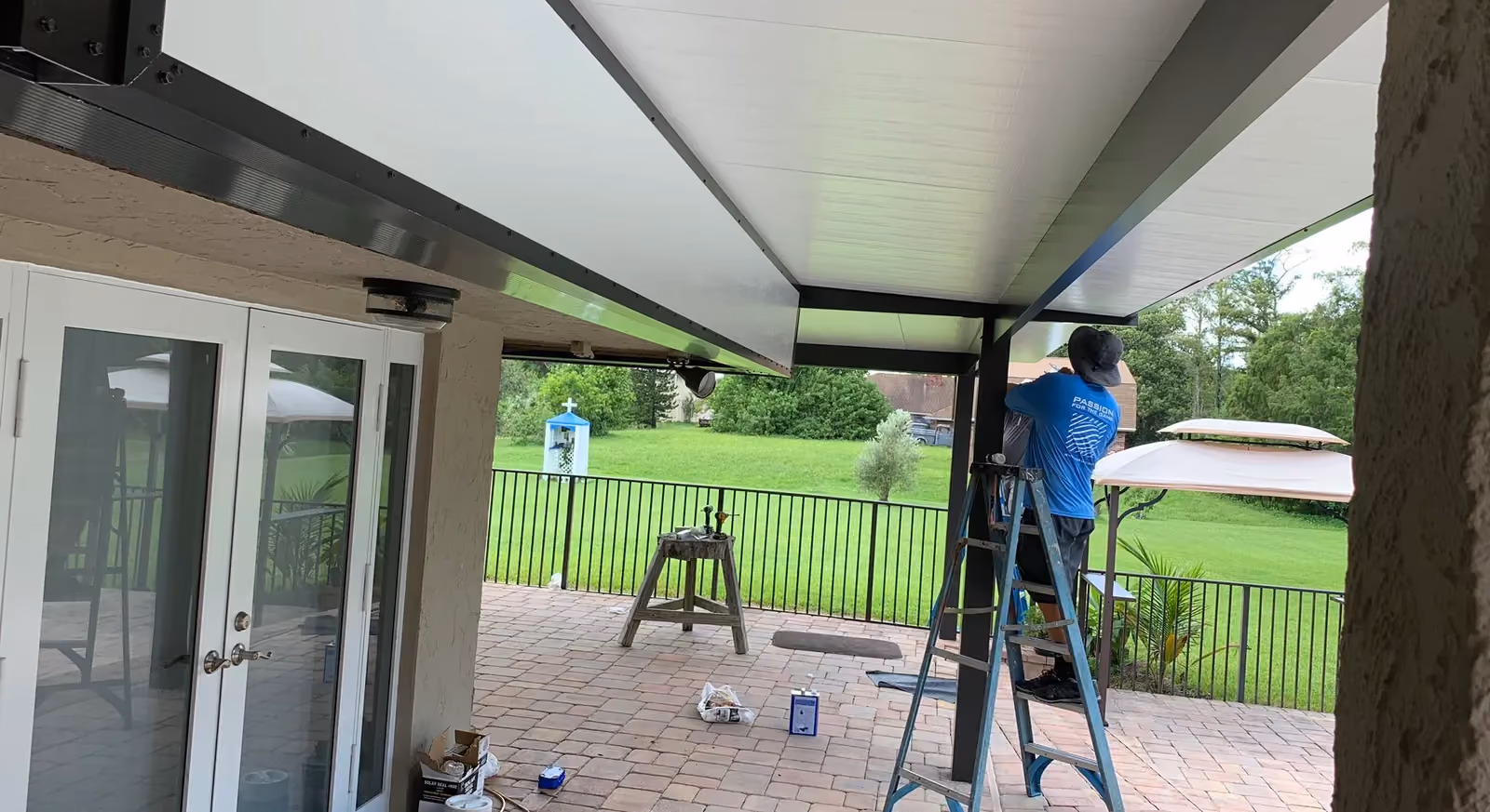 Underside of an insulated aluminum patio cover with bronze beams, installer on a ladder.