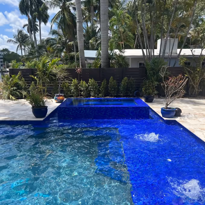 Pool with cobalt glass mosaic sun shelf, two bubblers and a raised tiled spa framed by royal palms.
