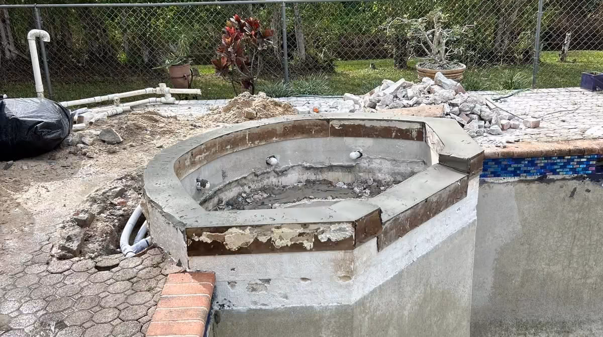 Spa with a newly poured concrete bond beam and exposed plumbing beside a drained pool, structural pool repair in Florida