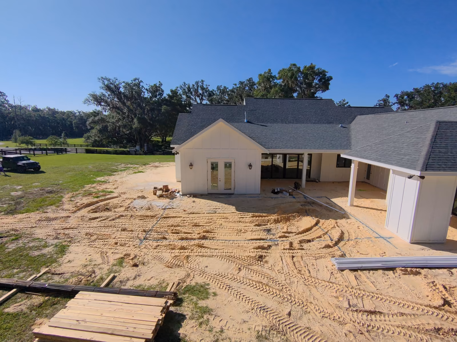 Backyard lot behind a new farmhouse with materials staged on the sand before excavation, custom pool construction in Florida