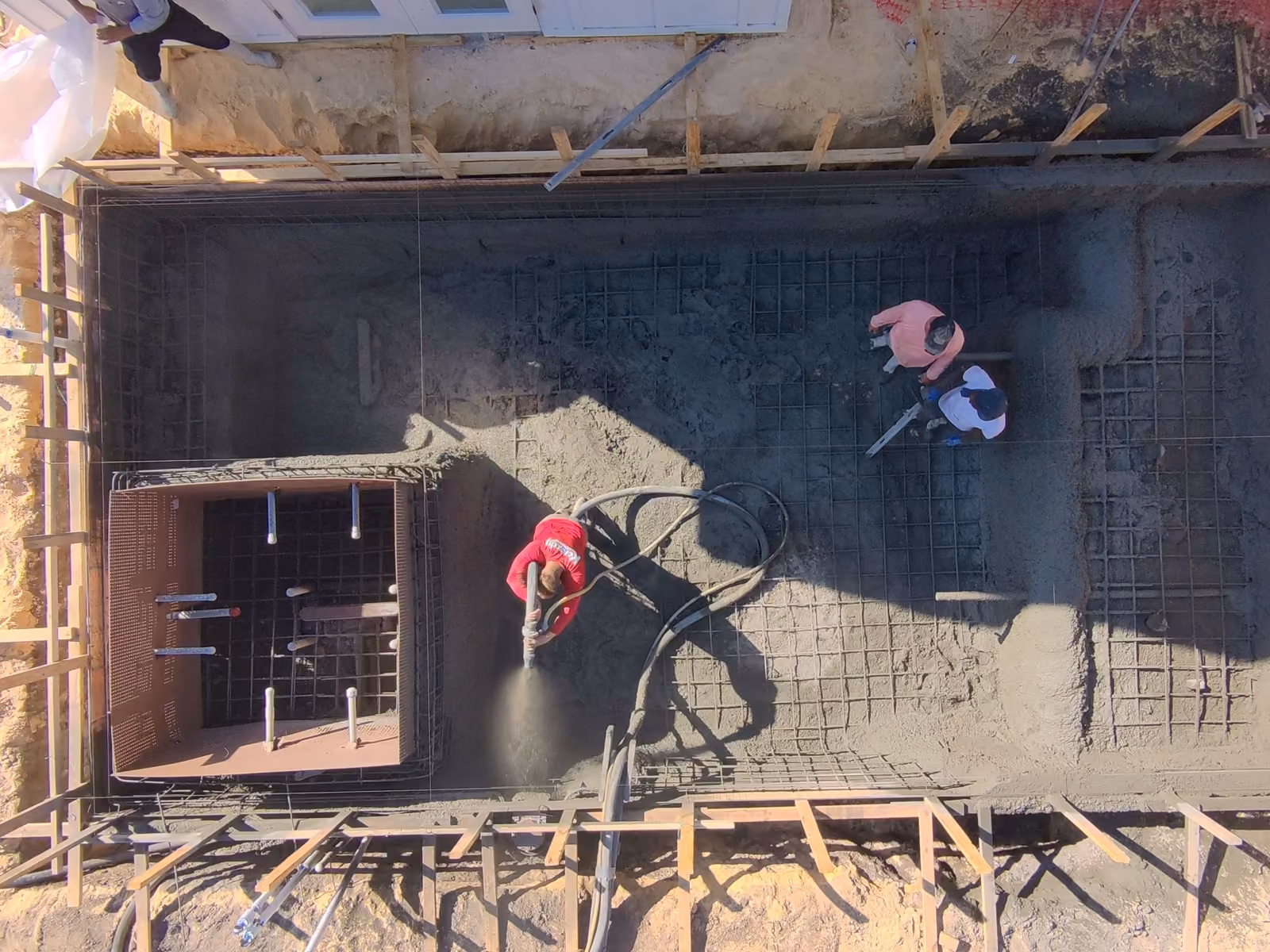 Top-down view of a crew spraying the gunite shell beside the spa form, custom pool construction in Florida
