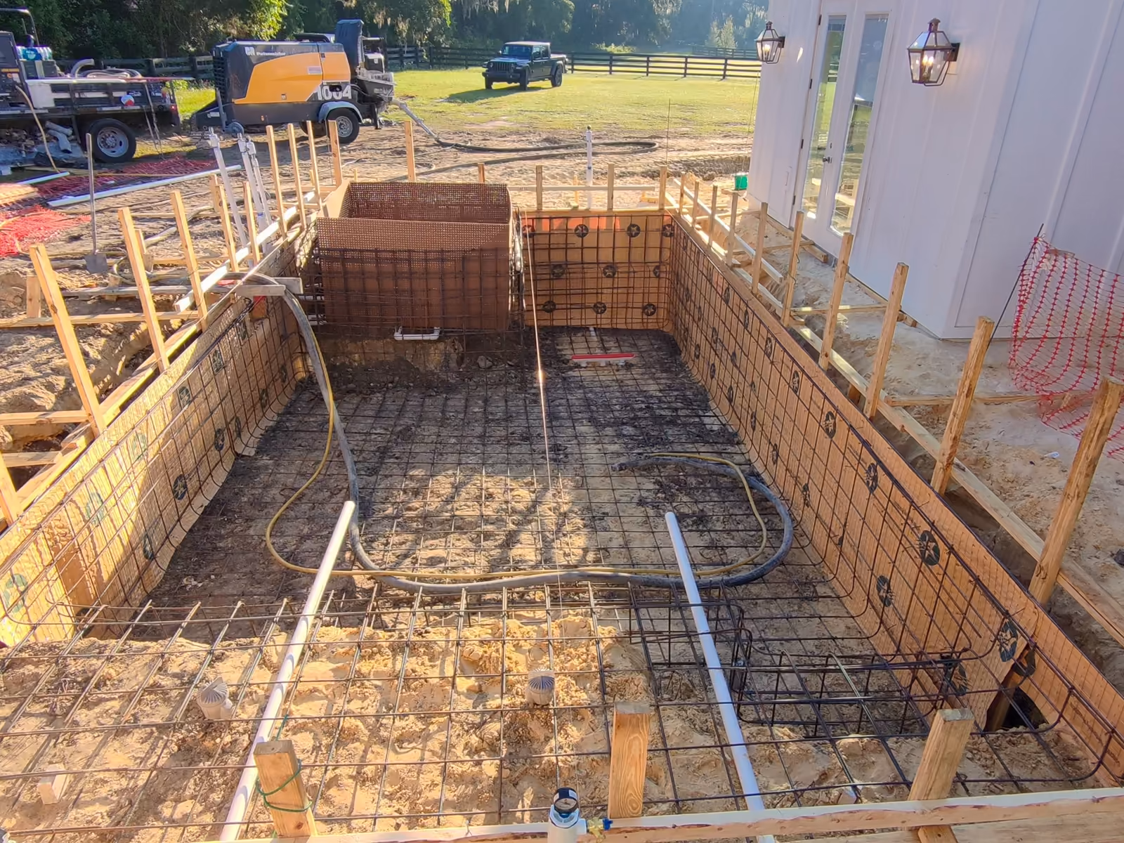 Steel rebar cage tied over wood forms with main drains and plumbing ready for inspection, custom pool builders in Florida