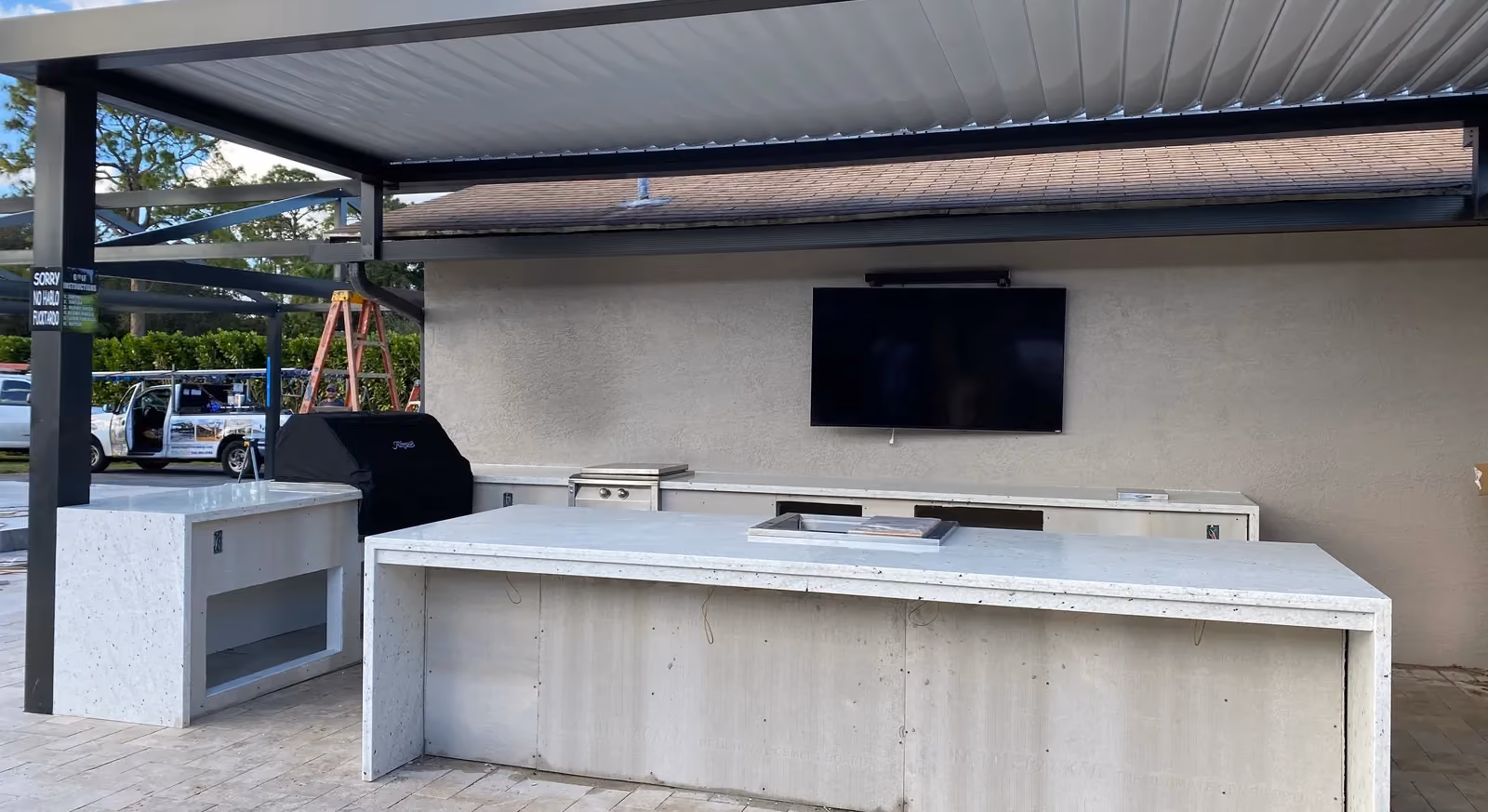 Outdoor kitchen under a louvered roof with granite countertops installed and cladding pending.