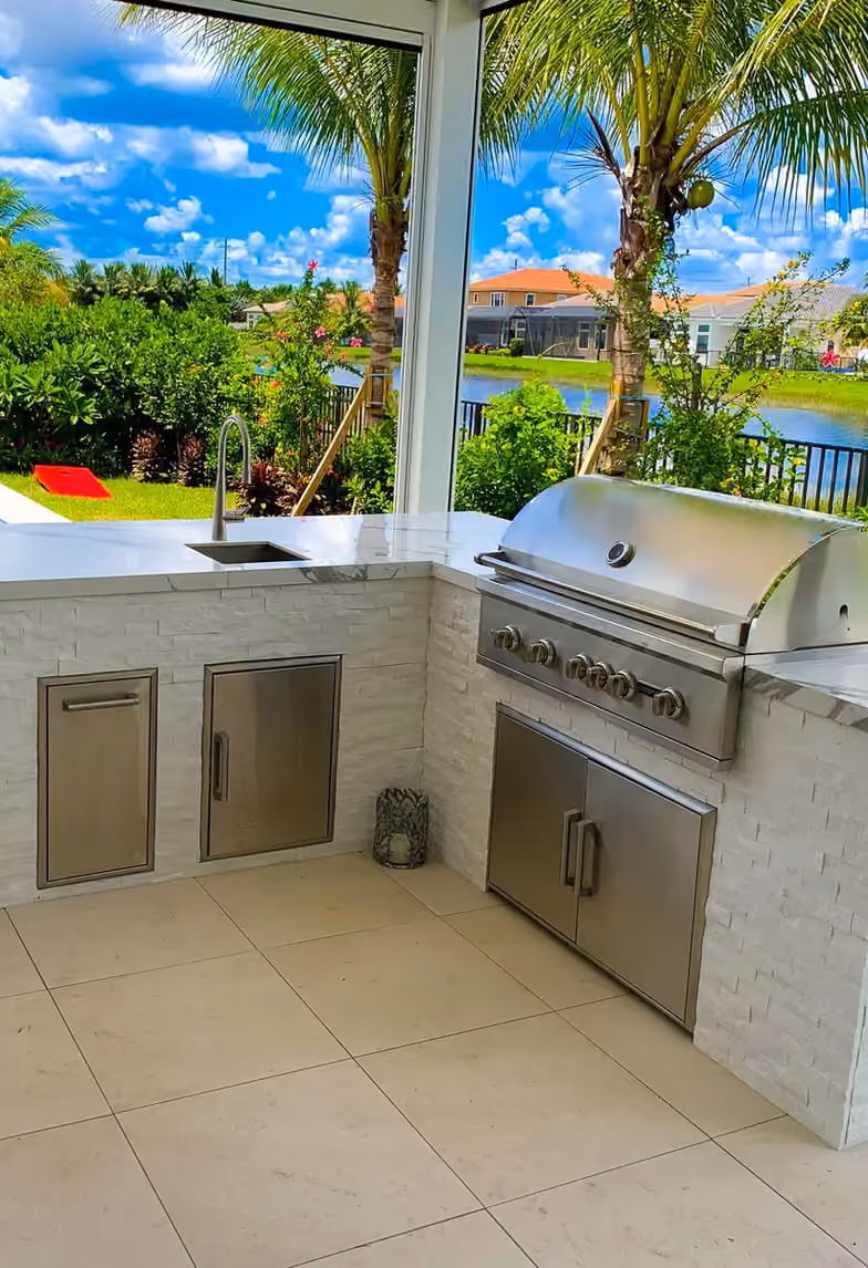 L-shaped outdoor kitchen in white stacked stone with built-in grill, sink and lake view.
