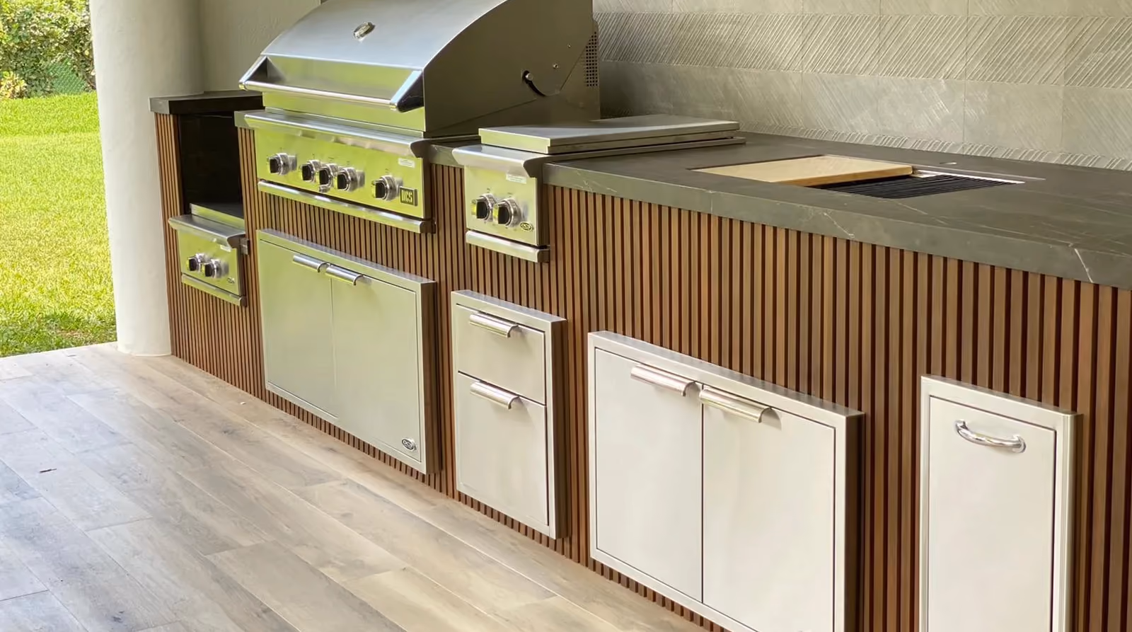 Outdoor kitchen with vertical wood slat cladding, stainless grill, side burner and access doors.