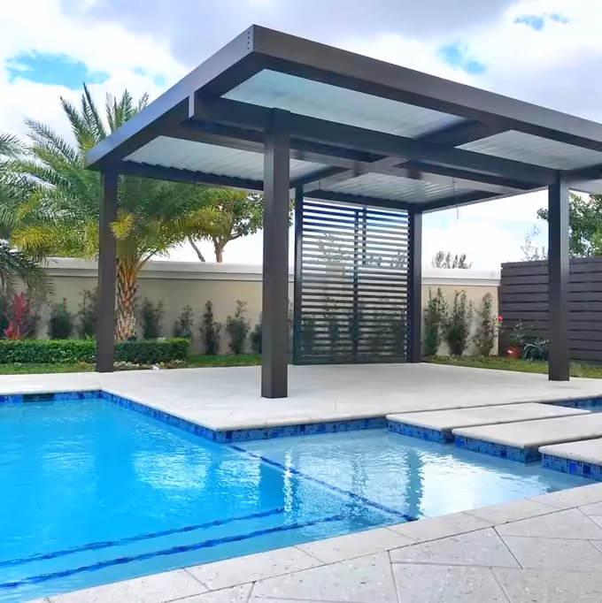 Freestanding dark aluminum patio cover with privacy screen on a pool deck with blue tile pool.