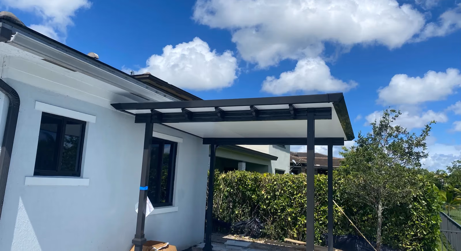 New black-framed insulated patio cover on a white house with marble pavers still being laid