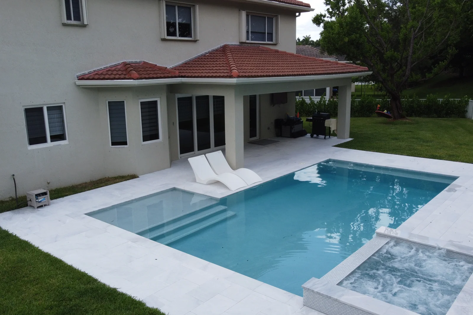 Aerial view of a backyard pool with raised spa and sun loungers