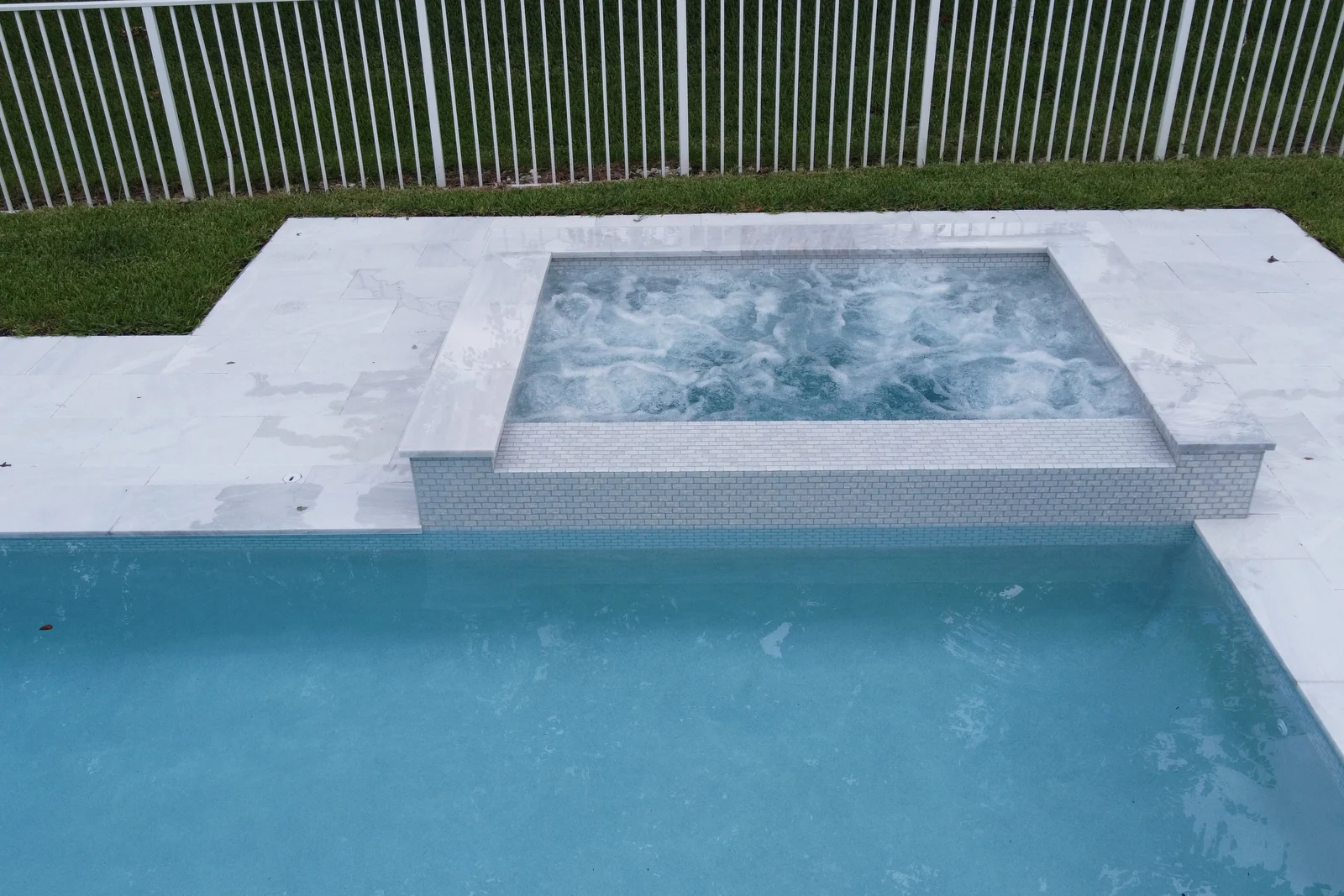 Aerial view of a backyard pool with a raised spa in pale mosaic