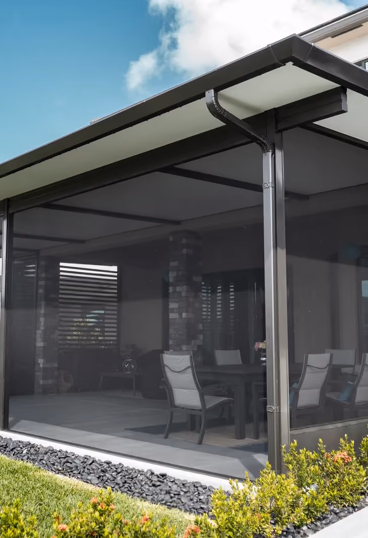 Dark-framed patio screen room under an insulated roof, with a dining set seen through the mesh.