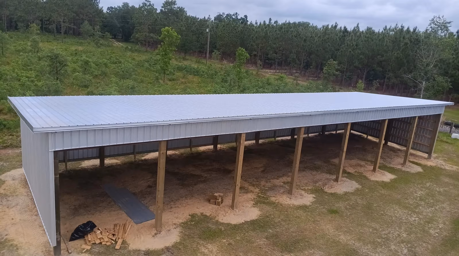Aerial view of a long single-slope pole barn with galvanized metal roof and open front bays.