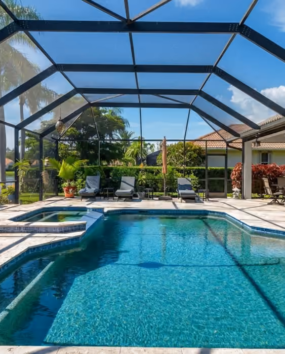 Dark-framed screen enclosure spanning a pool and spa, with loungers on the far deck.