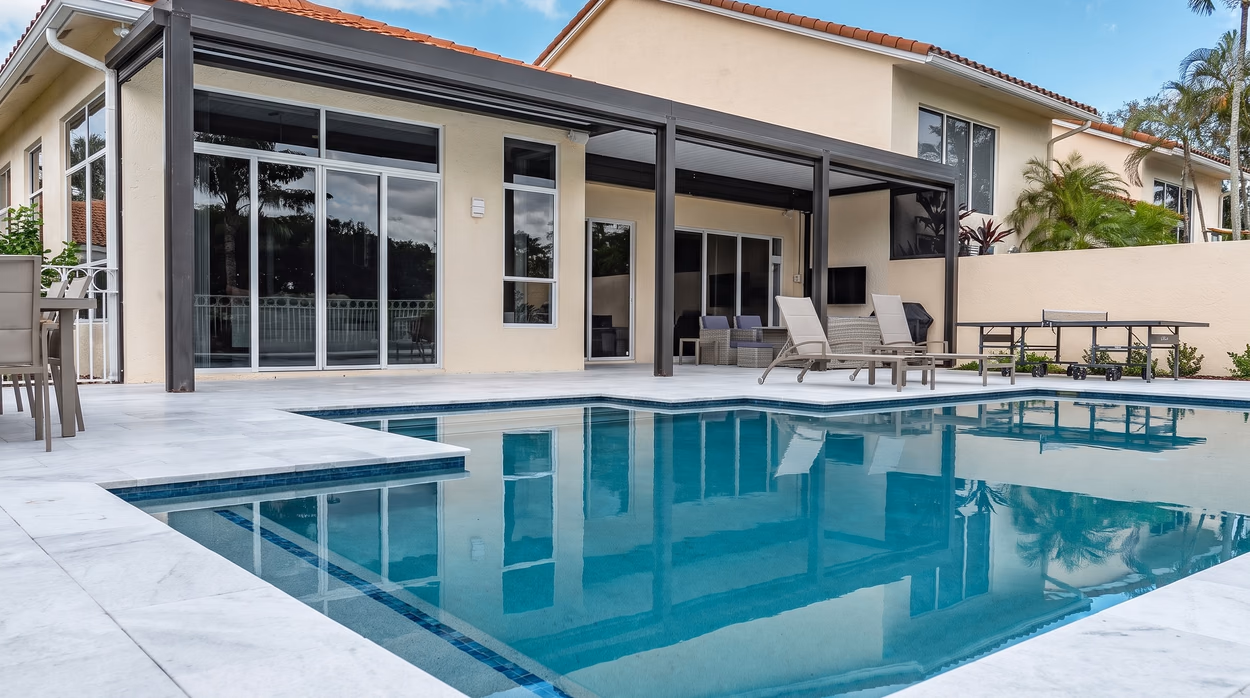Solid-roof aluminum patio cover running the full width of a South Florida home, beside the pool and marble deck.
