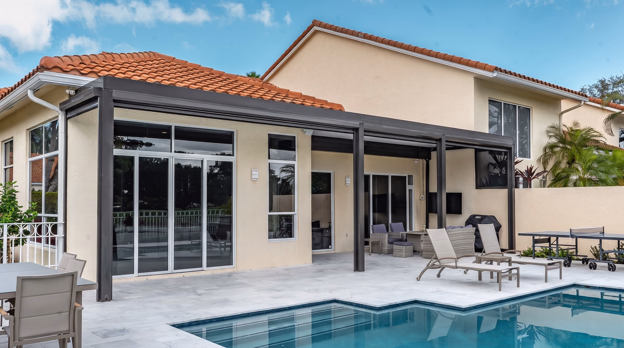 Pool and marble deck in the foreground with the aluminum cover and the barrel-tile roof of the home behind.