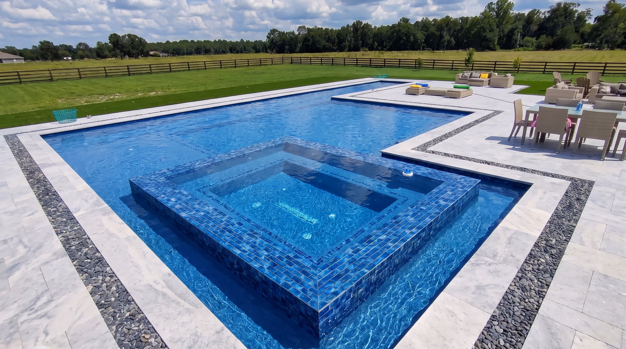 Raised spa clad in blue glass mosaic, spilling into the pool beside the outdoor lounge seating.