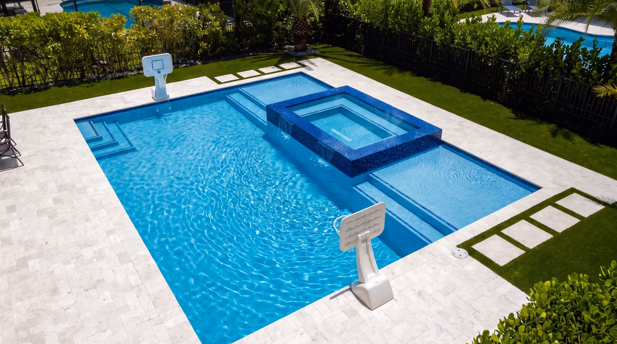 Overhead view of the pool, sun shelf and raised spa, with turf strips and paver steppers around the travertine deck.