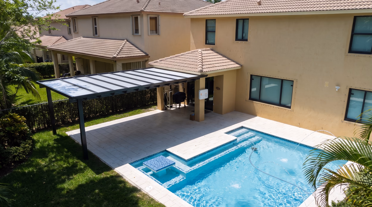 The pergola and pool seen from the lawn, with the two-story home and the hedge along the property line.