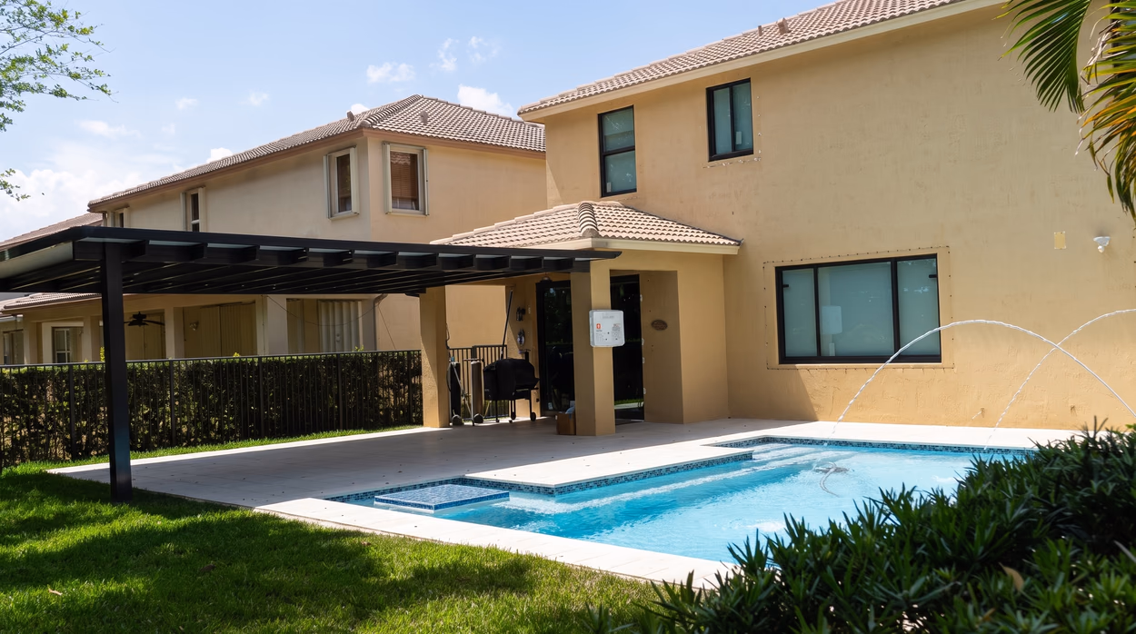 Deck jets arcing over the shallow end of the pool, with the pergola and the covered patio behind.