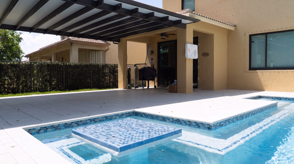 Raised spa clad in blue glass mosaic spilling into the pool, under the aluminum pergola.
