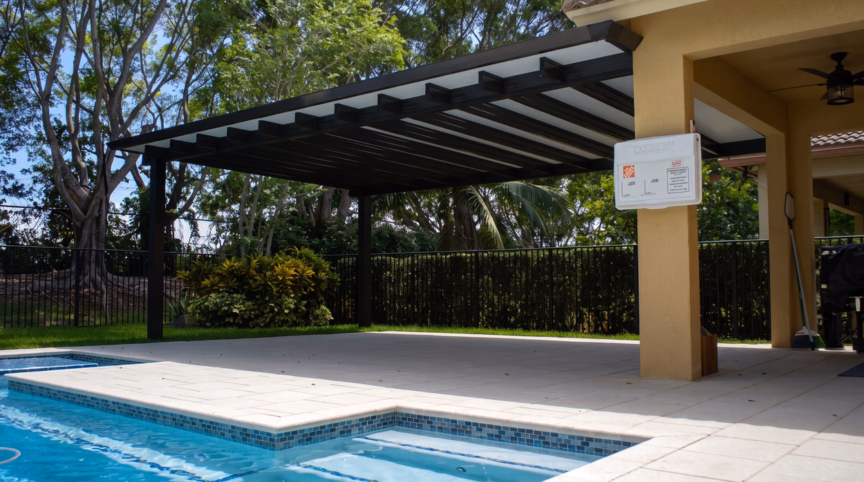 The aluminum pergola from beneath, framing the pool and the mature trees at the rear of the lot.