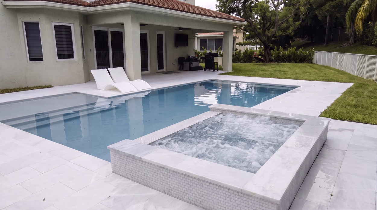 Pool with a raised white-tiled spa in the foreground and the covered lanai of the South Florida home behind.