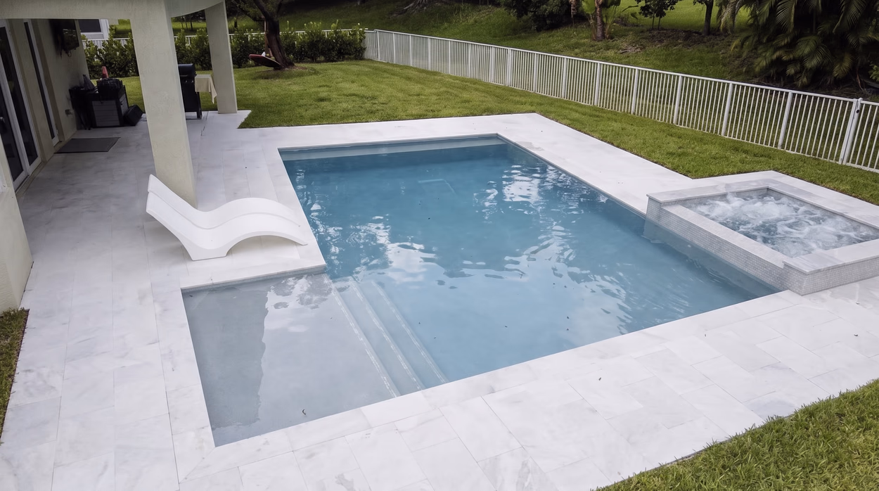 The pool seen along its length, with the sun shelf on the left and the white picket fence at the property line.