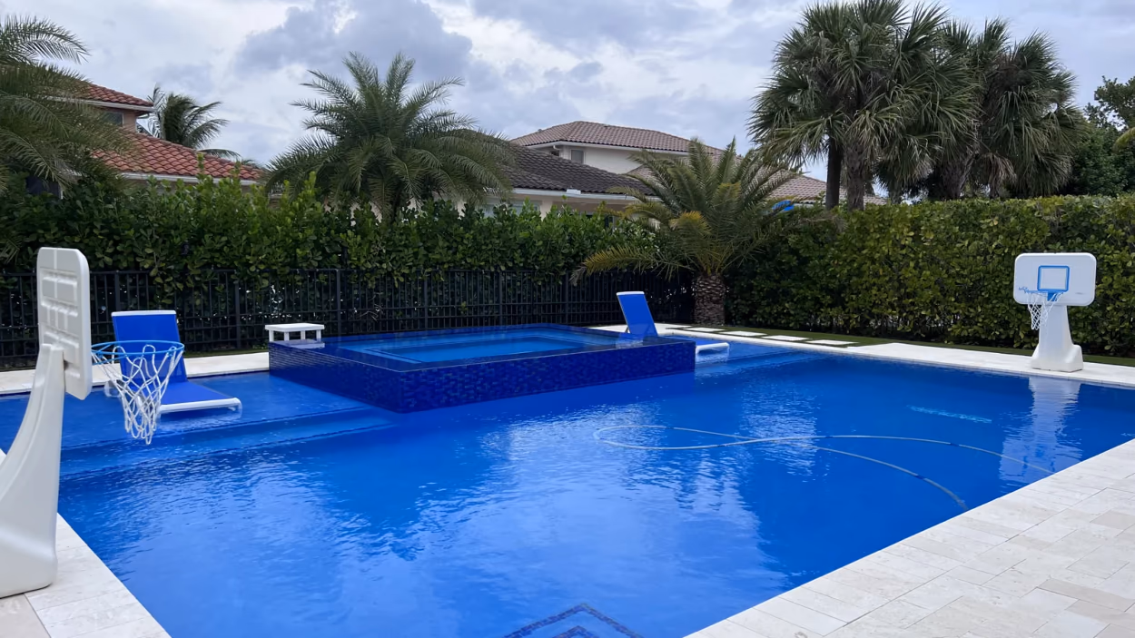 Remodeled pool with a raised spa clad in blue glass mosaic spilling into the water, on a travertine deck in Florida