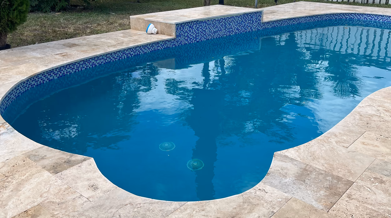 Blue glass mosaic waterline tile and travertine coping around a freeform pool in Florida